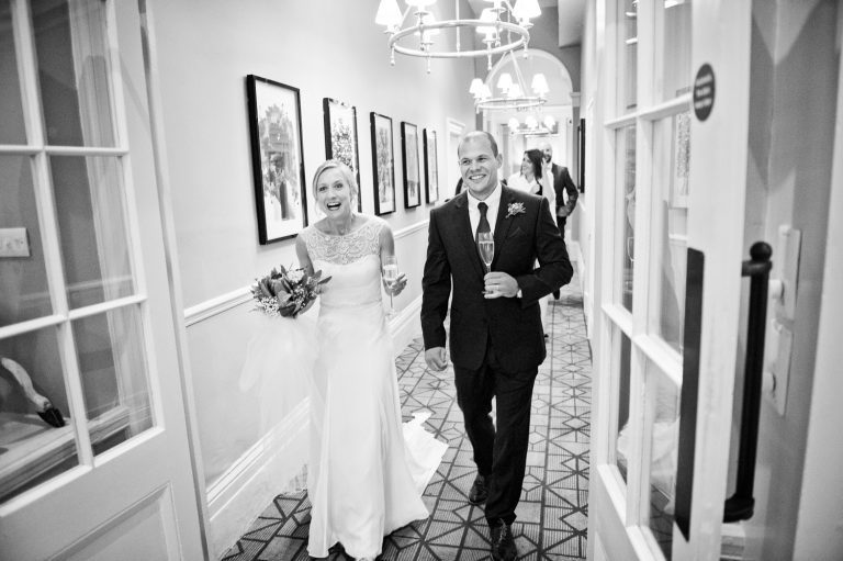 B&W photo of the bride and groom walking towards cheers from their wedding guests.