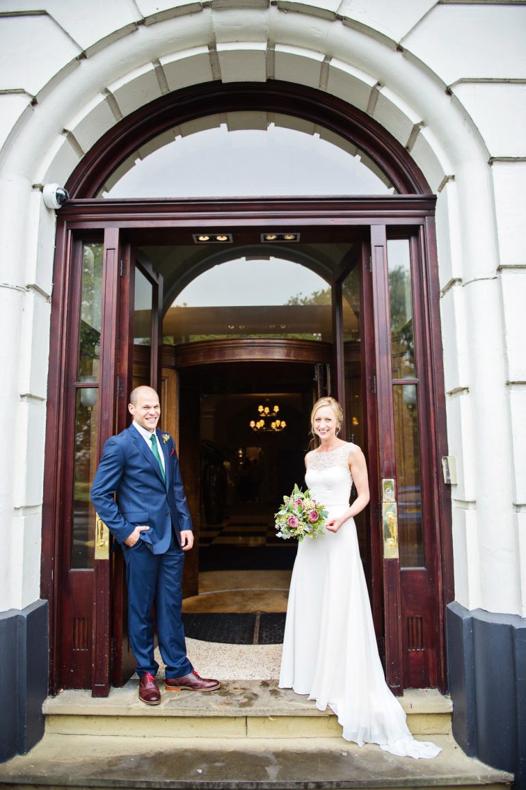 Bride and groom stand in front of the Queens Hotel.