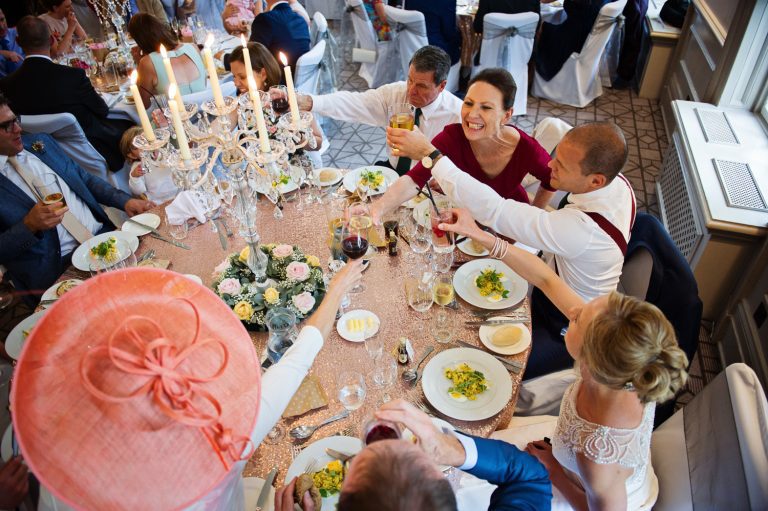 Candid photo of wedding guests at the breakfast table cheering each other at Queens Hotel, Cheltenham.