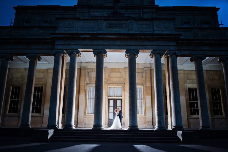 Night time shot of Pittville Pump Rooms, with the bride and groom. Pump Room pillars are lit up.