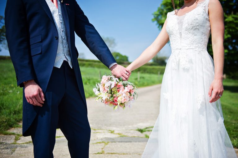 Bride and groom hold hands with the wedding bouquet in the centre.
