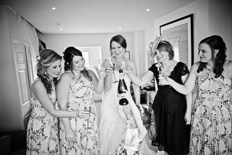 Team bride celebrate getting ready with a glass and bottle of fizz.