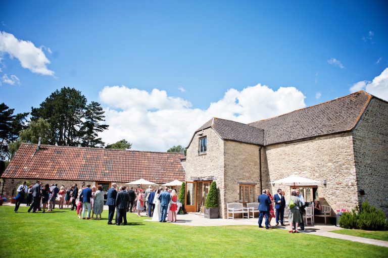 Overview of the garden at Kingscote Barn with wedding guests enjoying themselves and the sunny weather.