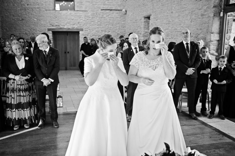 Two brides mopping their eyes during their wedding ceremony.