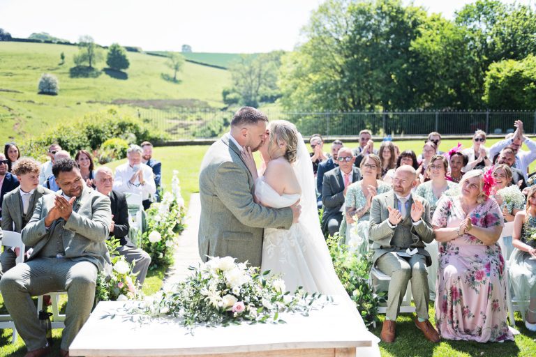 Candid moment of bride and groom kissing as they are announced husband and wife at their outdoor ceremony at Kingscote Barn.
