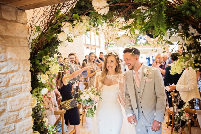 Bride and groom exit the ceremony after getting married at Kingscote Barn.