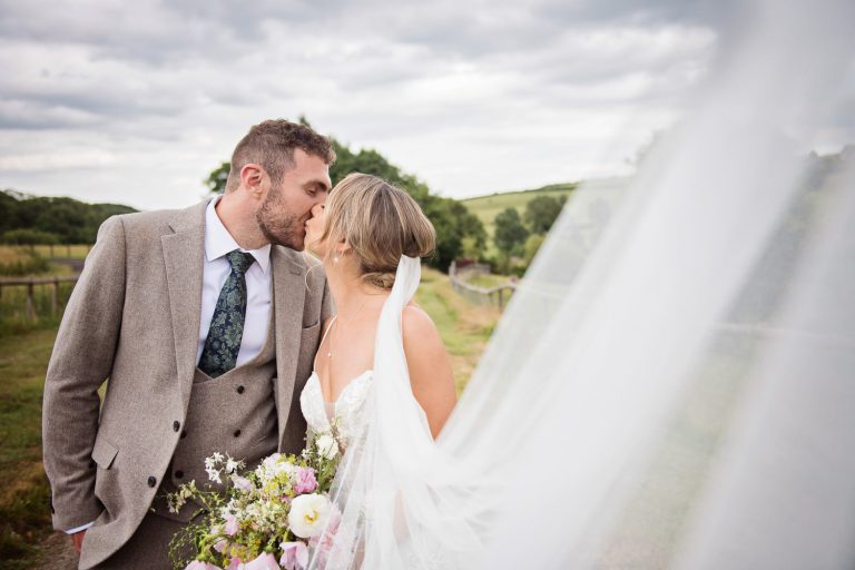 Bride and groom kiss by the wedding veil