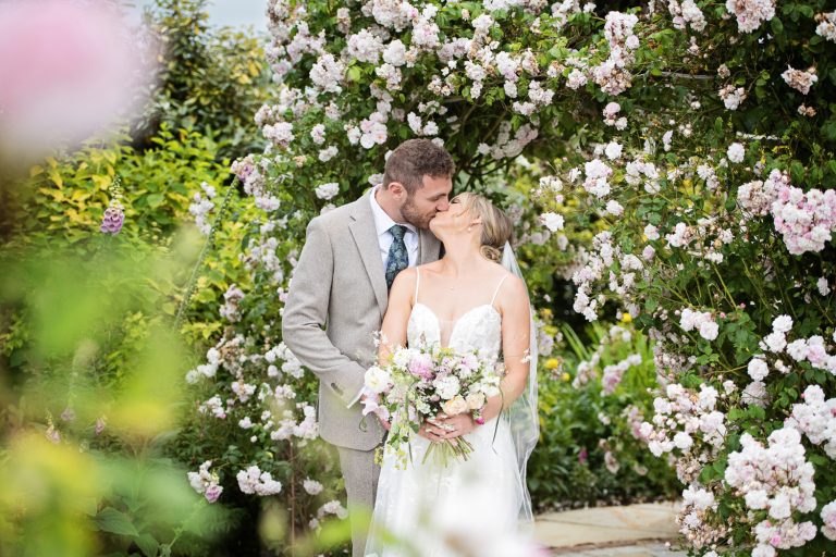Bride and groom kiss in the rose garden at Kingscote Barn.