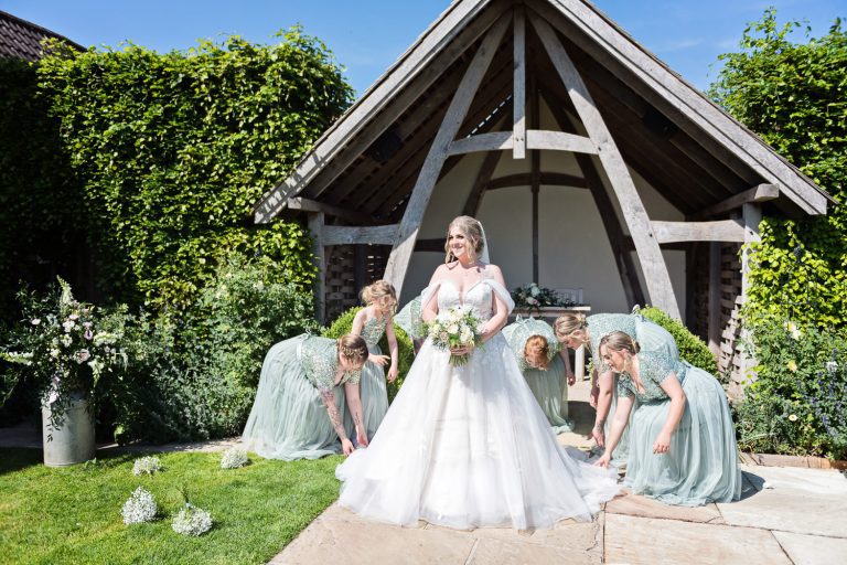 Bridesmaids tend to the brides wedding dress at Kingscote Barn.