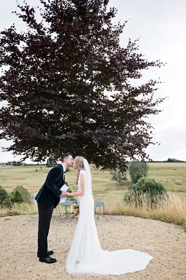 Bride and groom kiss after saying their private vows together at Kingscote Barn One Tree Hill