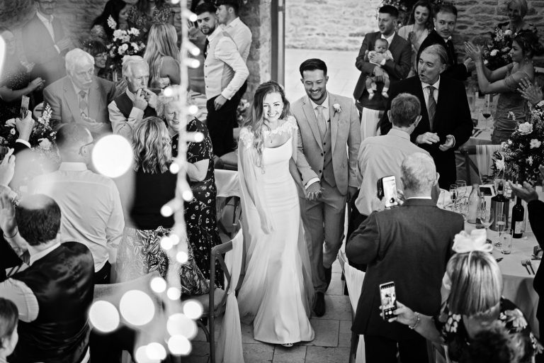 Bride and groom entering the wedding breakfast at Kingscote Barn.