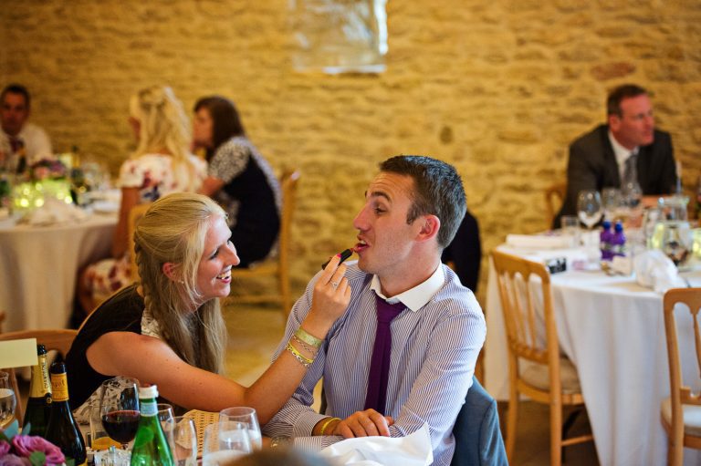 Fun candid photo of wedding guest (man) getting lipstick put on his lips at a wedding at Kingscote Barn.