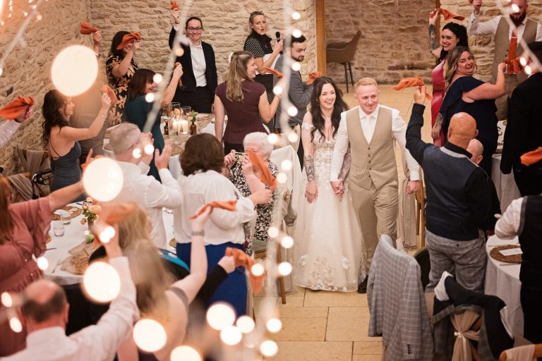 Wedding guests cheer the entrance of bride and groom as they enter the wedding breakfast.