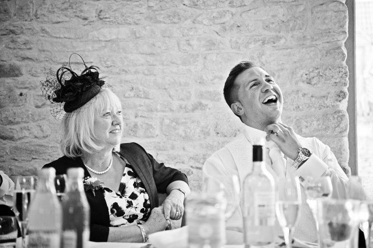 Story telling photo of Groom laughing but undoing his collar during wedding speeches.