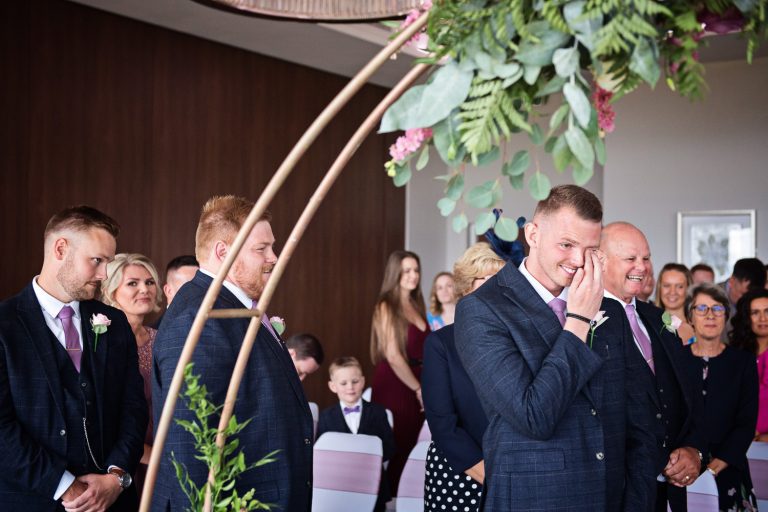 Documentary emotional moment of groom wiping is eyes as his bride is about to walk down the isle at a wedding at Tewkesbury Park.