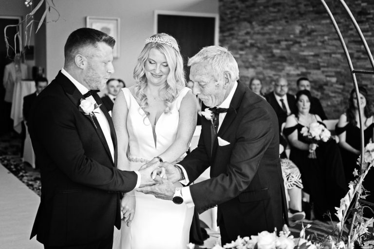 Candid moment of father of the bride handing over the brides hand to the groom whilst getting married at Tewkesbury Park