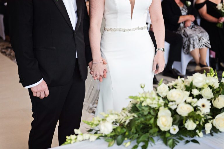 Candid moment bride and groom holding hands whilst getting married at Tewkesbury Park