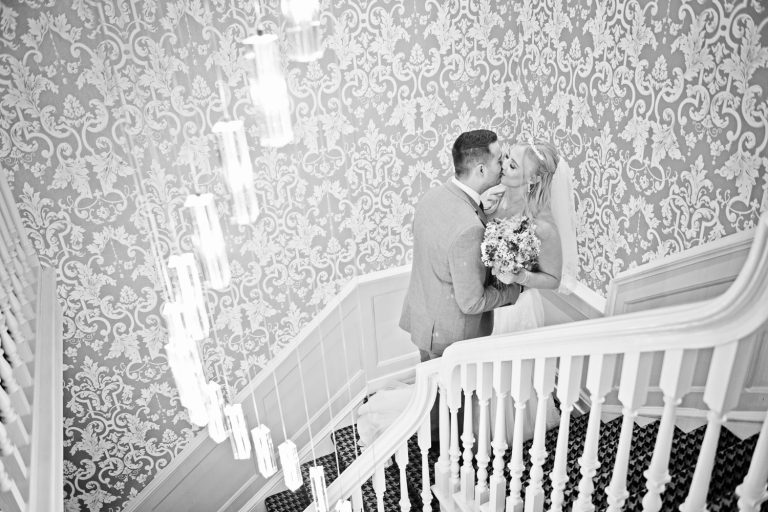 Bride and groom kiss on the stairway at Tewkesbury Park. B&W image.