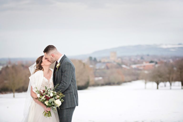 Bride and groom kiss in the gorgeous grounds at Tewkesbury Park with a winter backdrop (snow).