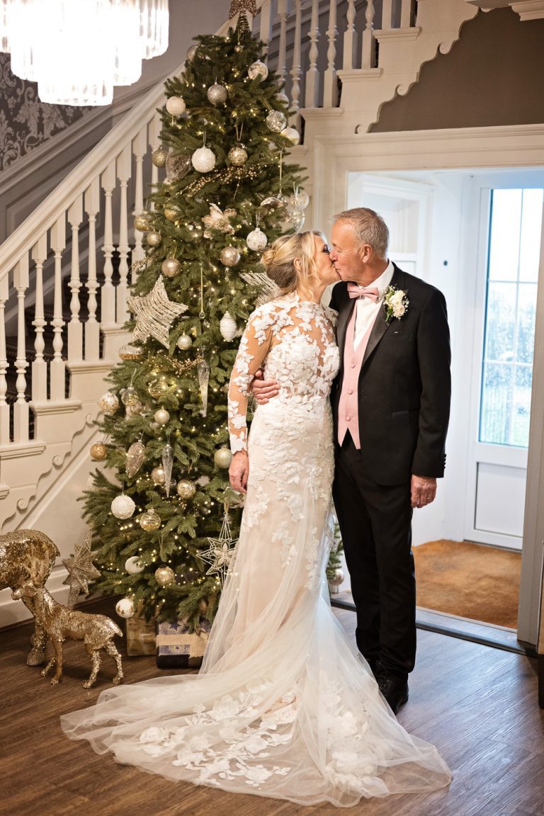 Bride and groom kiss in front of a Christmas Tree at Tewkesbury Park Hotel.