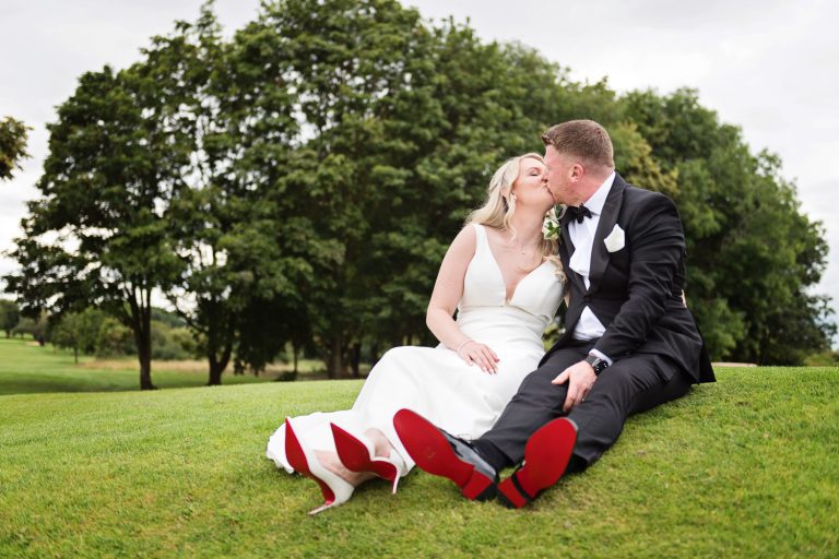 Bride and groom kiss in the gorgeous grounds at Tewkesbury Park. Red soles on shoes.