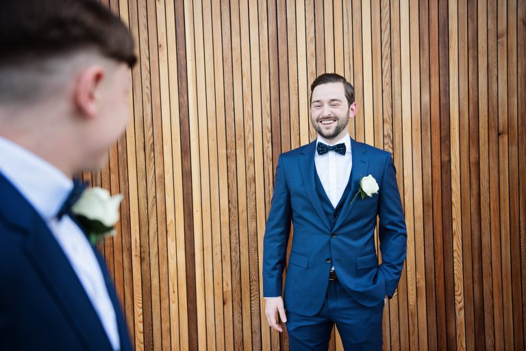 Groom poses in front of a wooden cedar wall for a wedding at Tewkesbury Park Hotel.