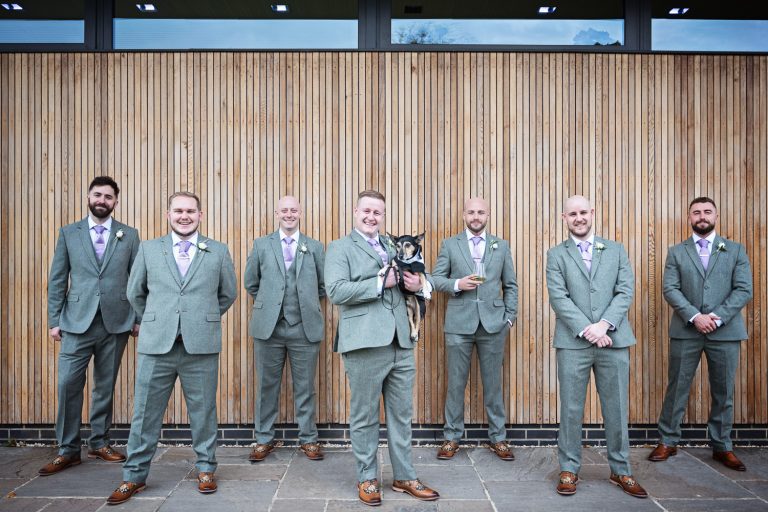 Groom his dog and groomsmen pose in front of a wooden cedar wall for a wedding at Tewkesbury Park Hotel.